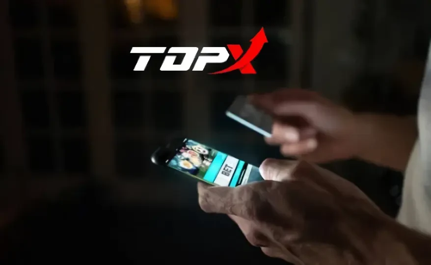 Mãos segurando um celular no escuro, com o logotipo da TopX